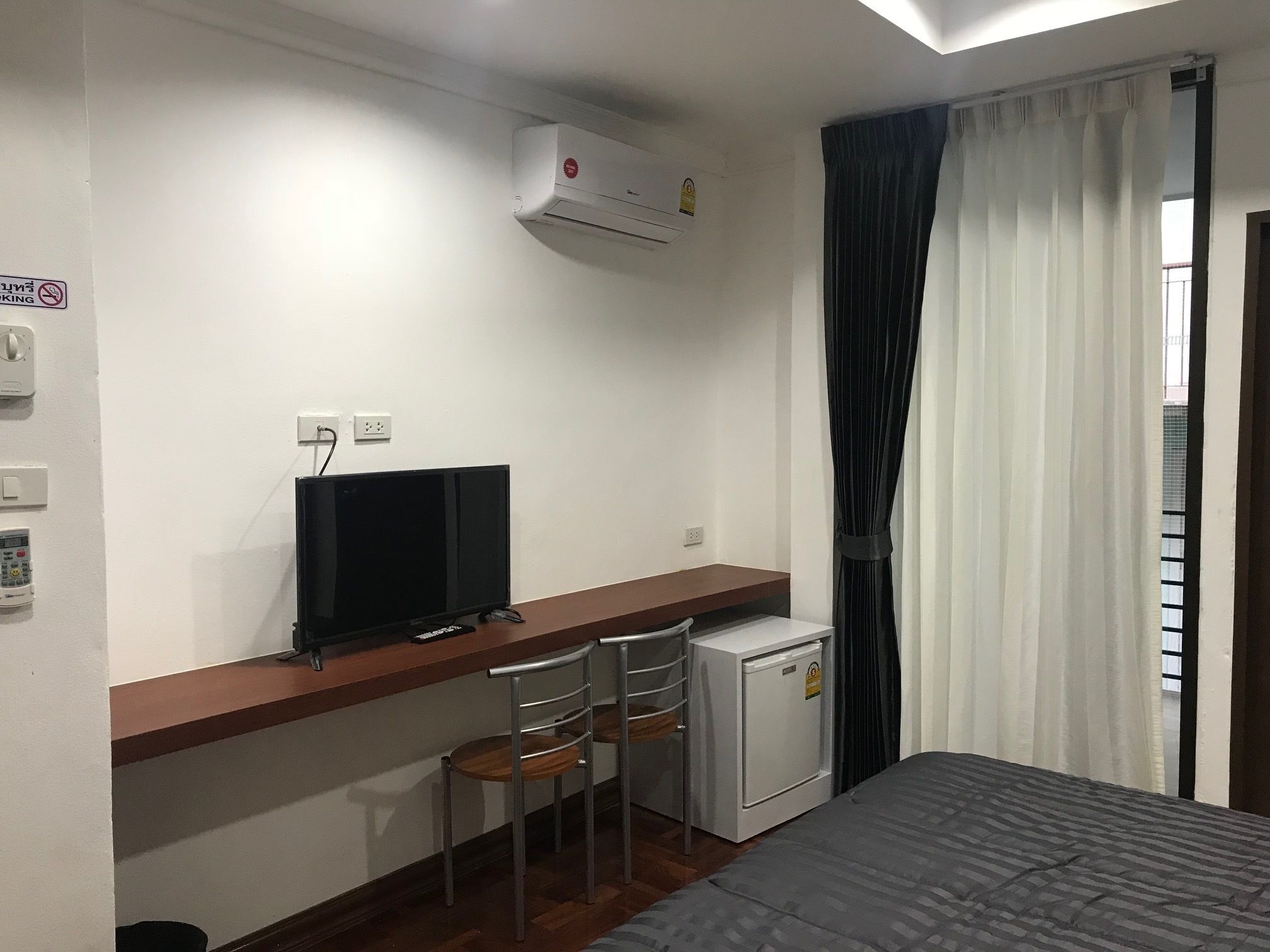 A hotel room with a bed, a desk with a TV, a mini-fridge, and a window with curtains.