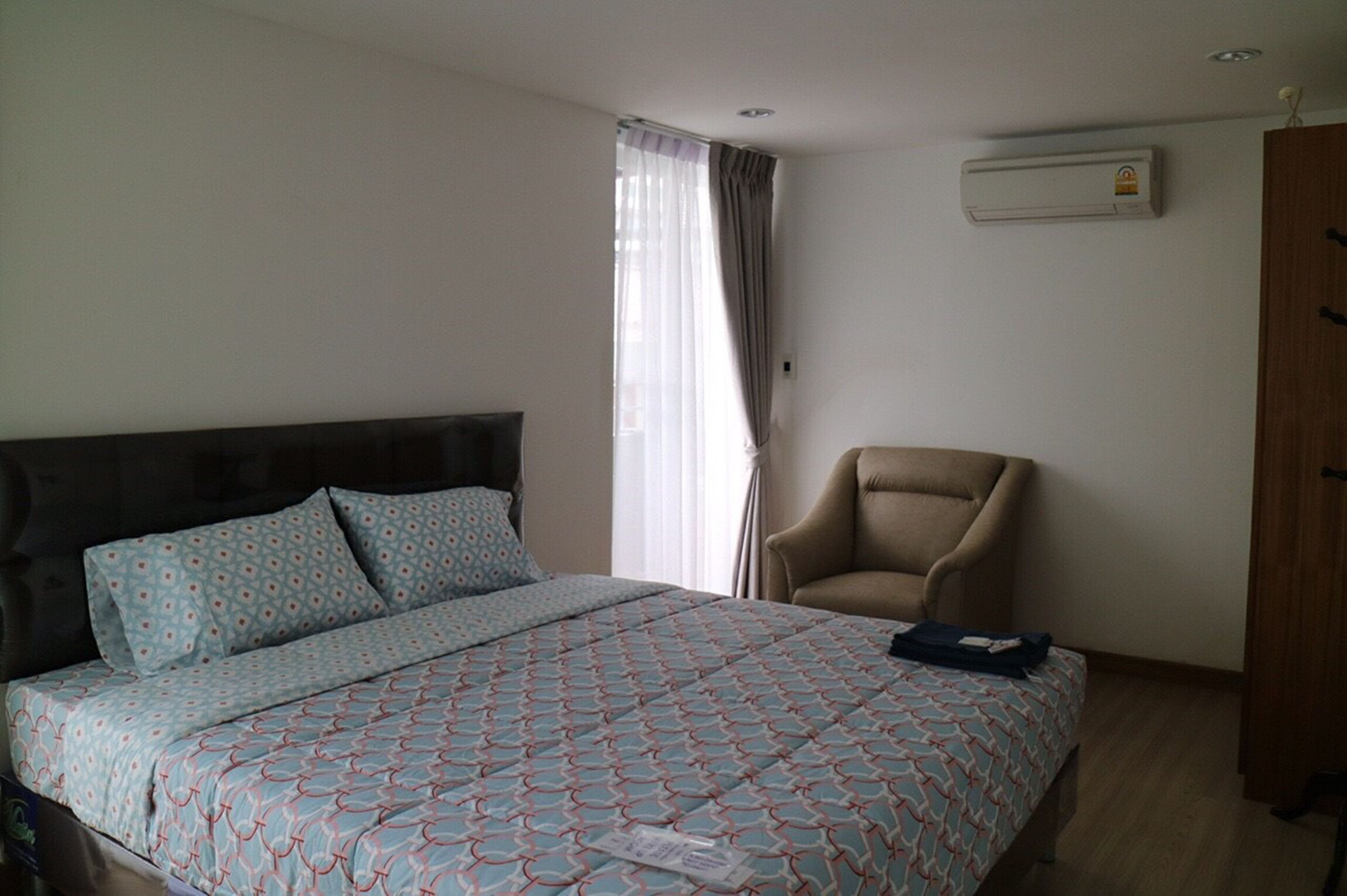 Un dormitorio con cama, una silla, un armario y aire acondicionado.
