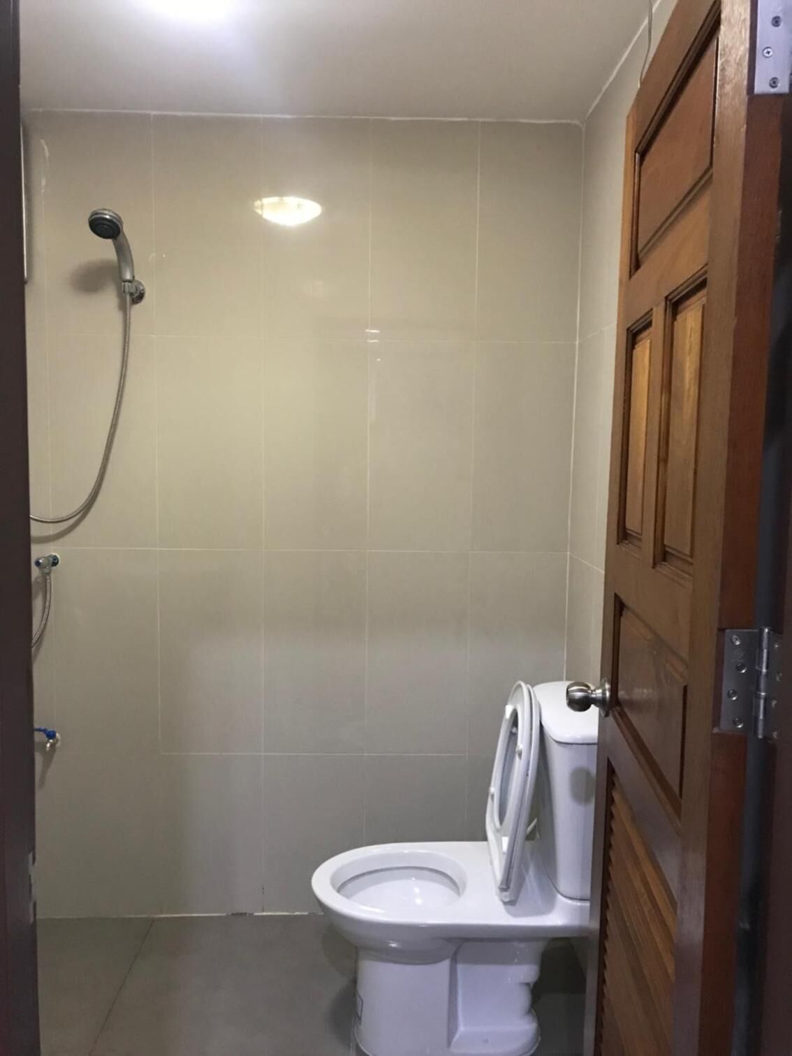 A small, private bathroom with a toilet, a shower, and a wooden door.