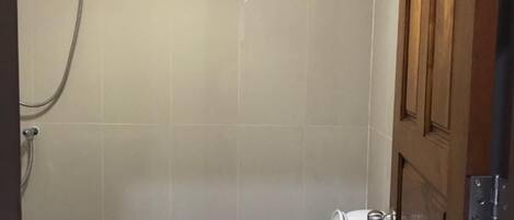 A small, private bathroom with a toilet, a shower, and a wooden door.