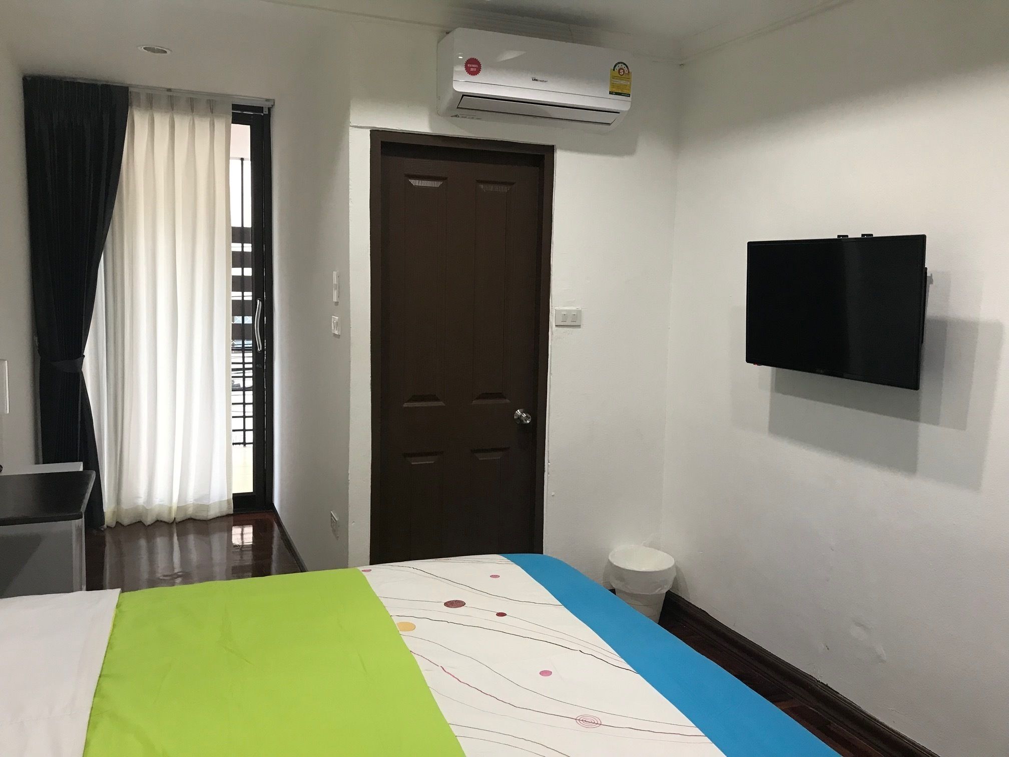 A hotel room with a bed, a TV mounted on the wall, a door, and an air conditioning unit.