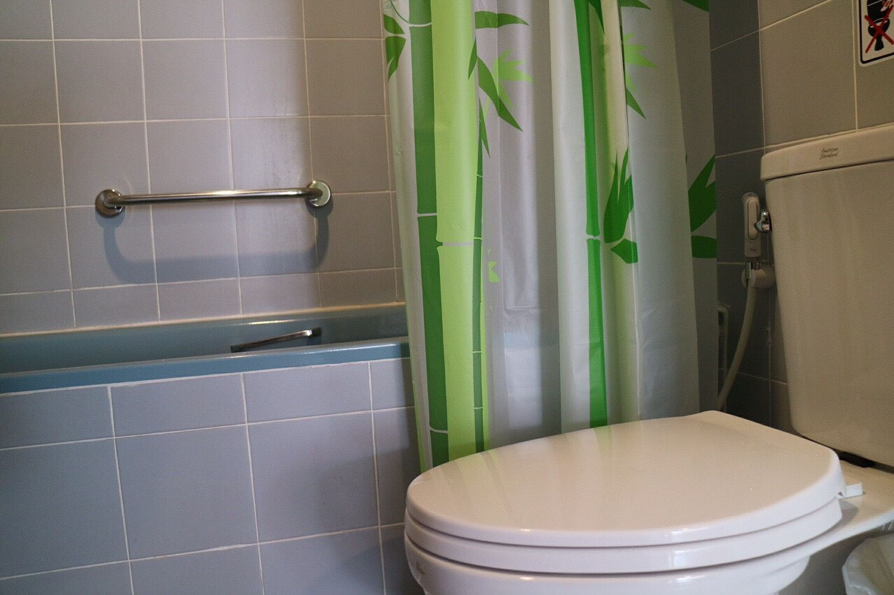 A bathroom with a white toilet, a grab bar, and a shower curtain with a bamboo design.
