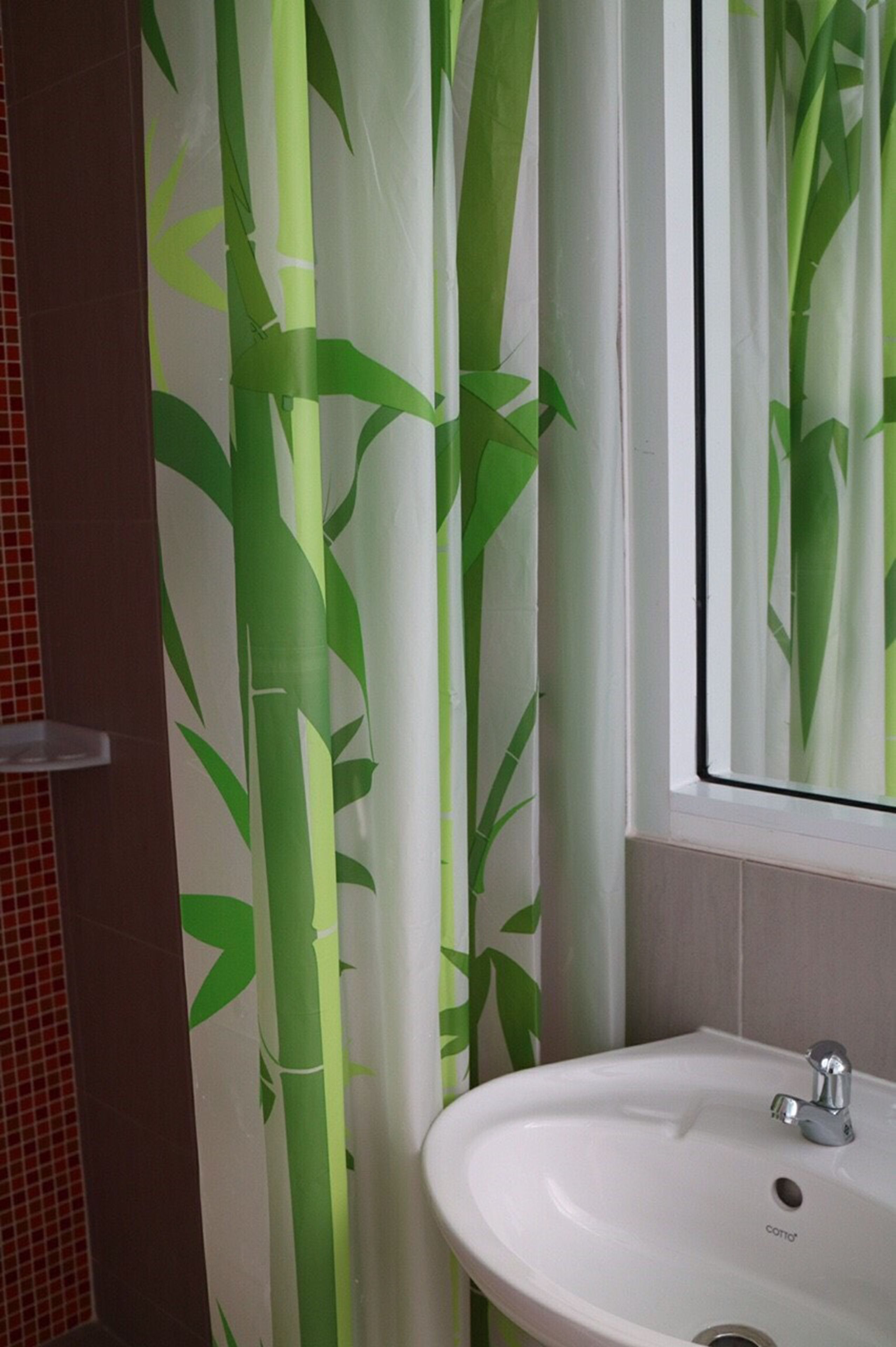 A bathroom with a white sink, a mirror, and bamboo-themed curtains.