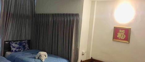 A bedroom with two beds, a wooden chair, and a wall-mounted light fixture.