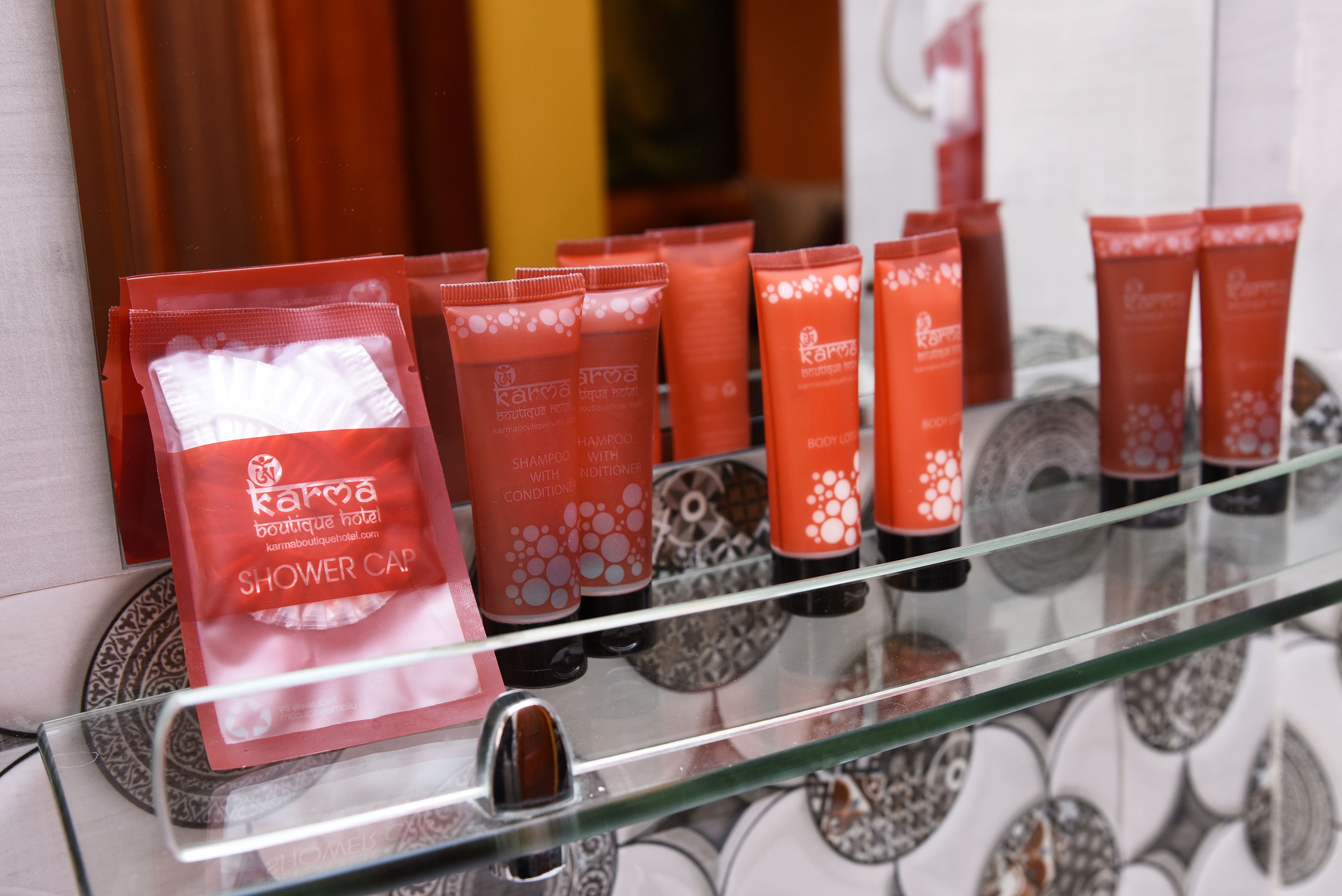 En glashylde med forskellige røde og hvide badeværelsesprodukter, herunder brughætter og shampoo- samt conditionerflasker.