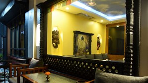 Una habitación tradicional con un banco de madera, una mesa con un florero, y un espejo grande que refleja una estatua de Buda y un cuadro.