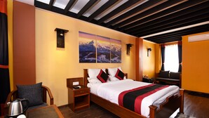 Una habitación de hotel con una cama de madera, una mesita de noche, una mesa con cafetera y un cuadro en la pared.