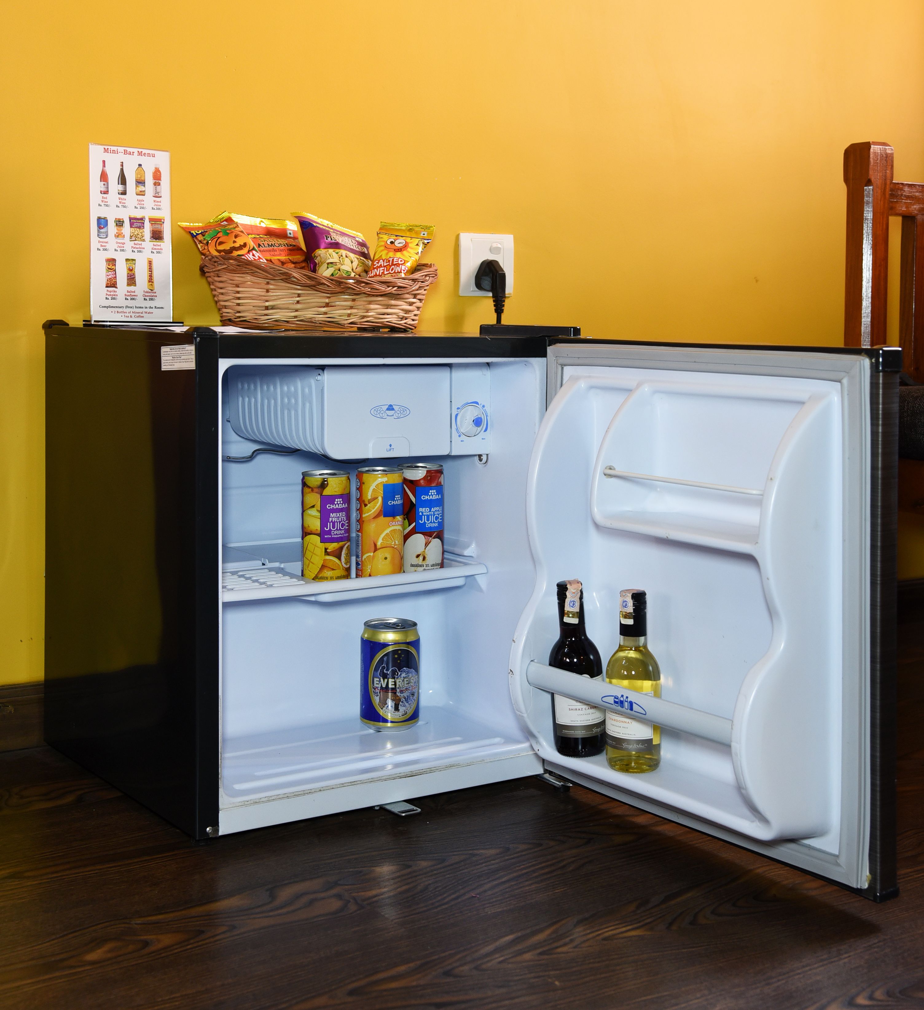Un minibar con carta, diferentes bocadillos y bebidas, incluyendo latas y botellas.