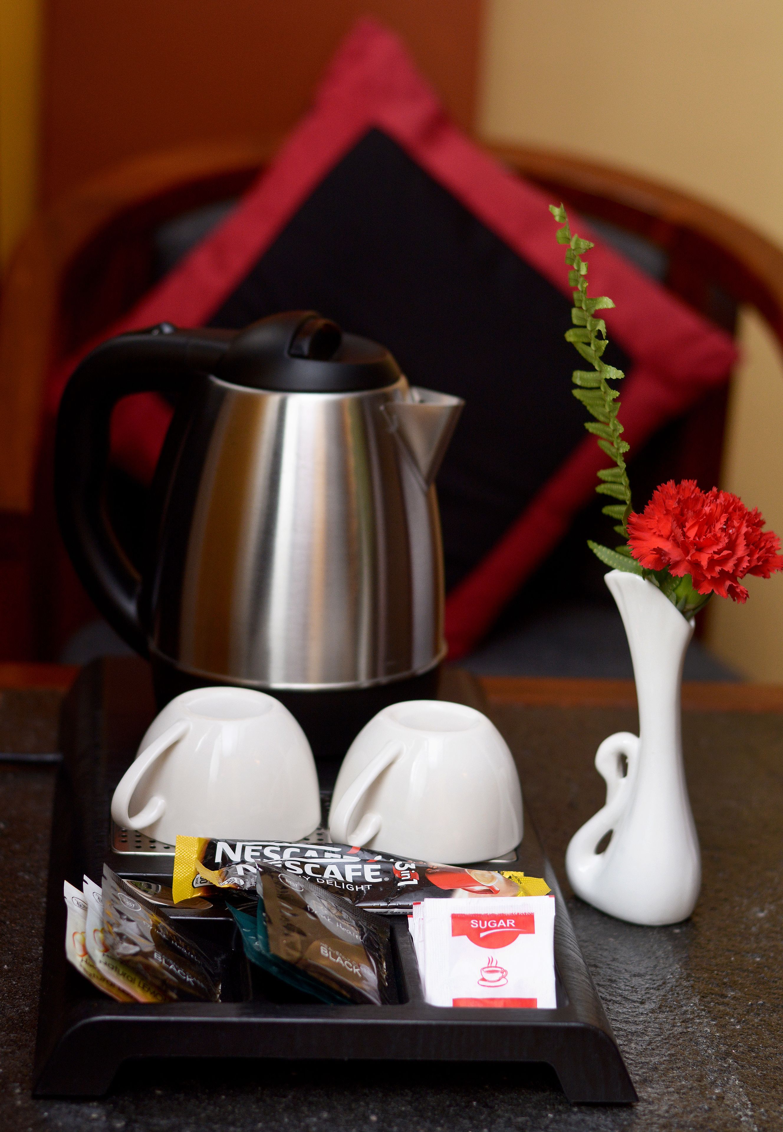 A tray with a coffee maker, two cups, a vase with flowers, and coffee packets.