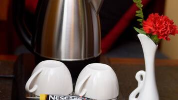 A tray with a coffee maker, two cups, a vase with flowers, and coffee packets.