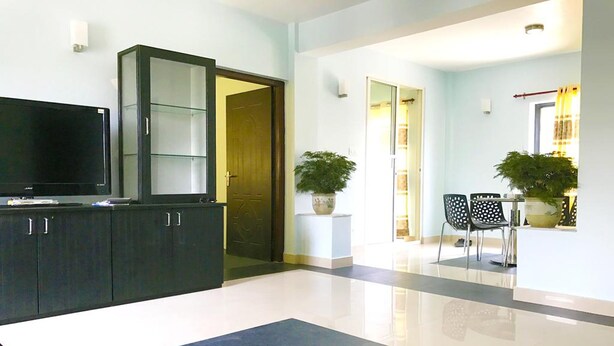 A modern living room with a flat-screen TV, dark cabinets, a large rug, and a dining area with chairs and a table. - Lazimpat Luxury Apartments (Kathmandu)