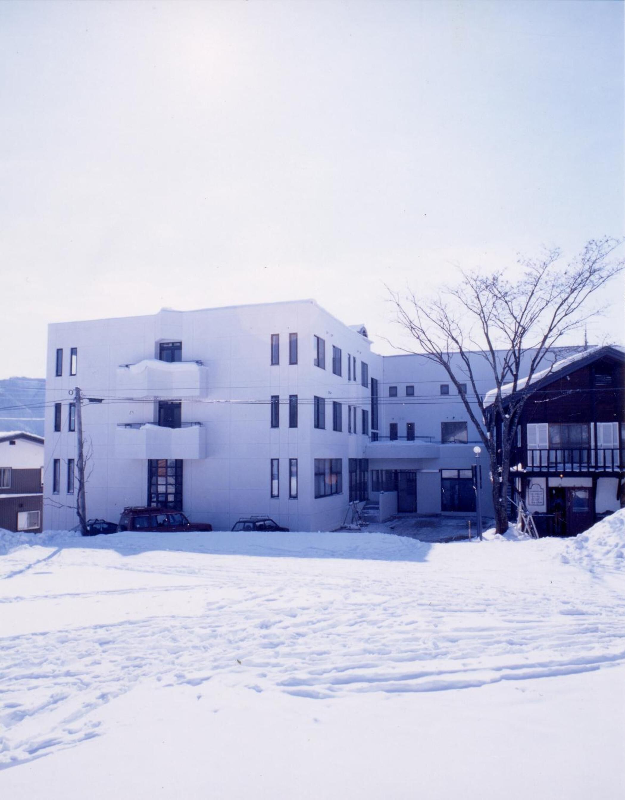 A modern white building with multiple windows and a flat roof, surrounded by snow.
