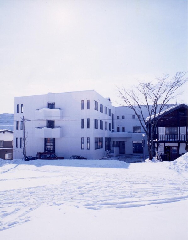 A modern white building with multiple windows and a flat roof, surrounded by snow.