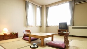 Ein traditioneller japanischer Raum mit Tatami-Boden, einem niedrigen Tisch, zwei gepolsterten Stühlen, einem Fernseher und einer Heizung.