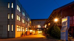 Ein Hotel mit modernem Design, das einen zentralen Eingang mit Glasüren, zahlreiche Fenster und eine gut beleuchtete Fassade aufweist.