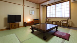 Ein traditioneller japanischer Raum mit Tatami-Böden, einem niedrigen Tisch, einem Fernseher und einem großen Fenster.