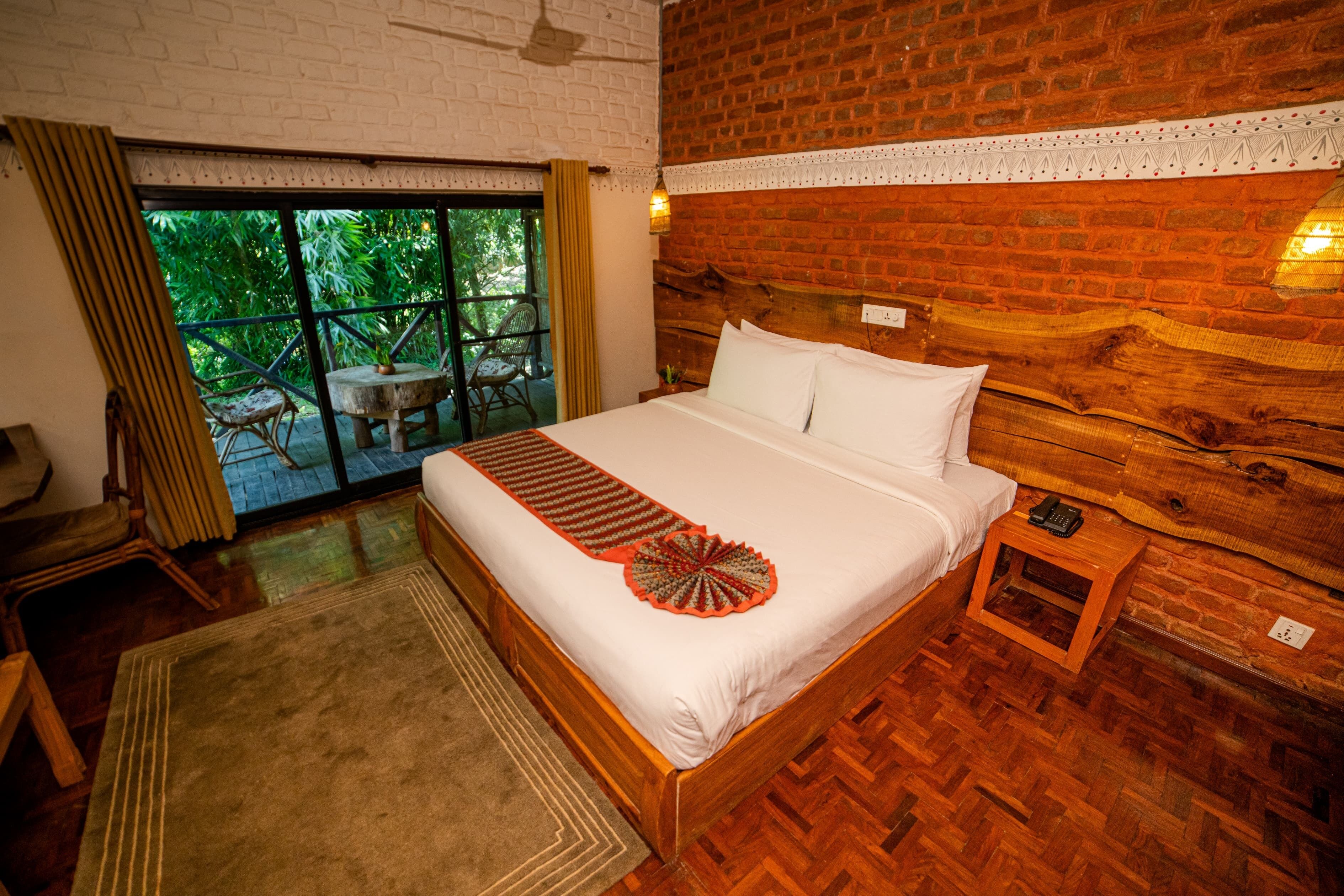 Une chambre à coucher avec un lit en bois, une table de chevet, une petite table et une vue sur la verdure grâce à une grande fenêtre.
