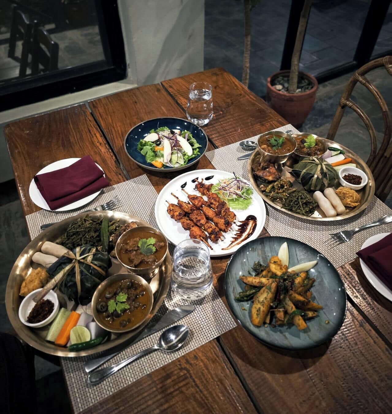 Ein Holztisch mit mehreren Tellern Essen, einem Glas Wasser und einem Blumentopf.