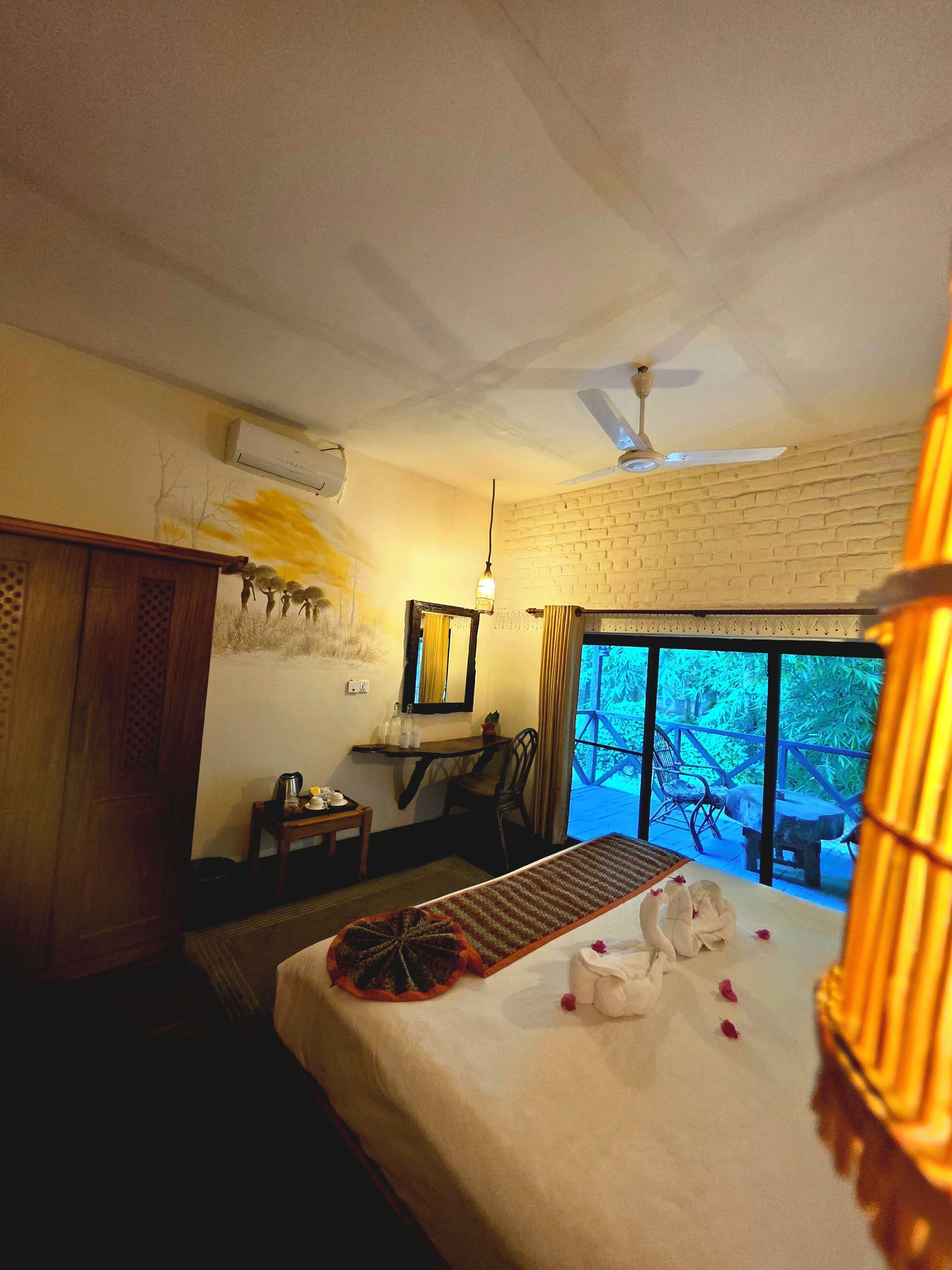 A hotel room with a bed, a desk, a chair, a window with a view, and a ceiling fan.