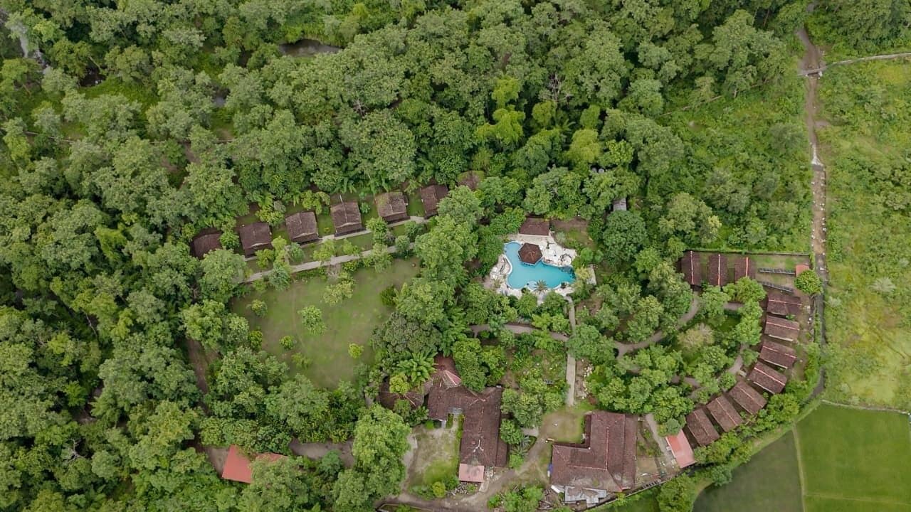 An aerial view of a resort with a swimming pool surrounded by lush greenery and multiple bungalow-style buildings.