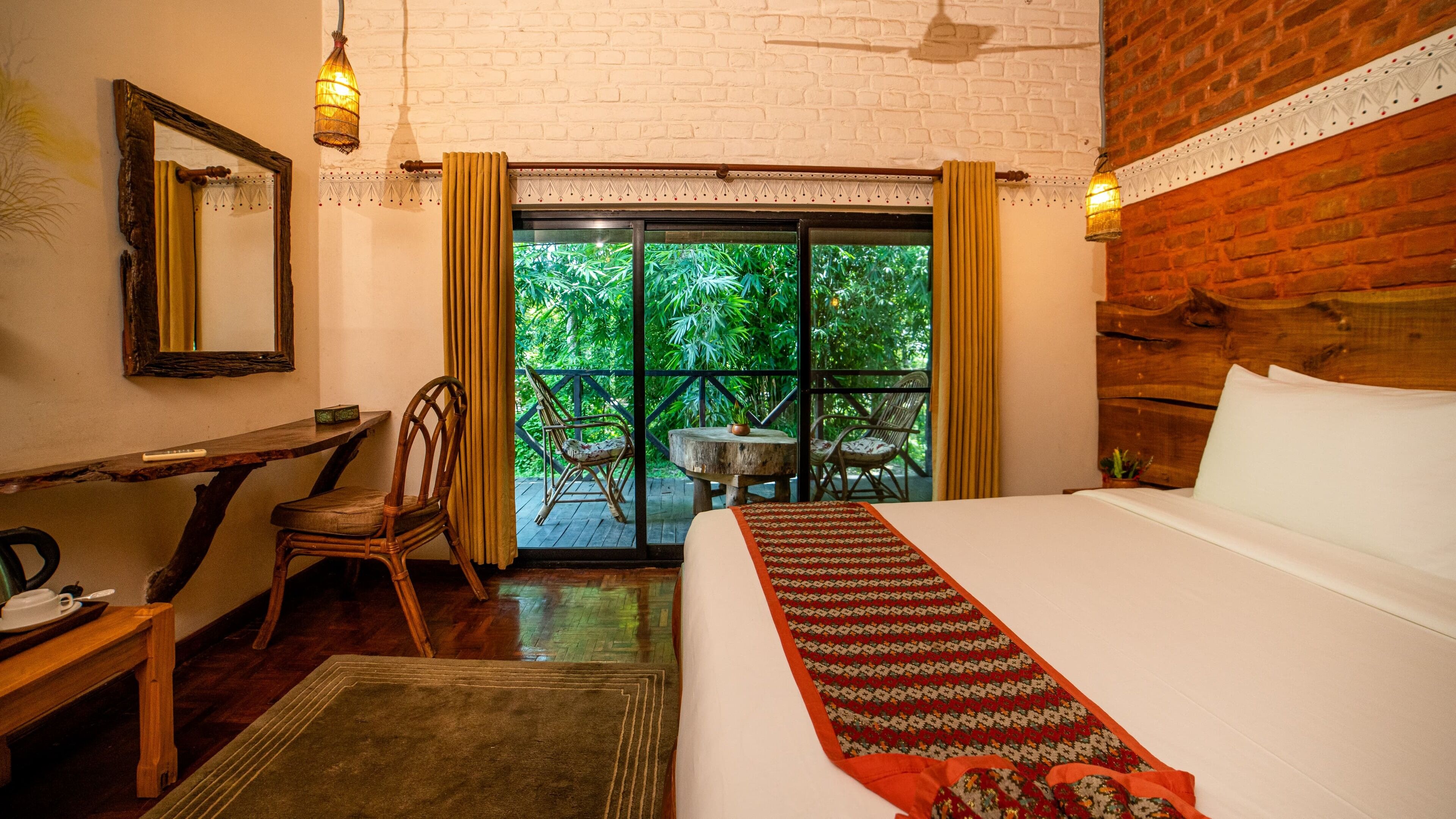 A hotel room with a bed, a desk, a chair, a small table, and a view of greenery through the window.