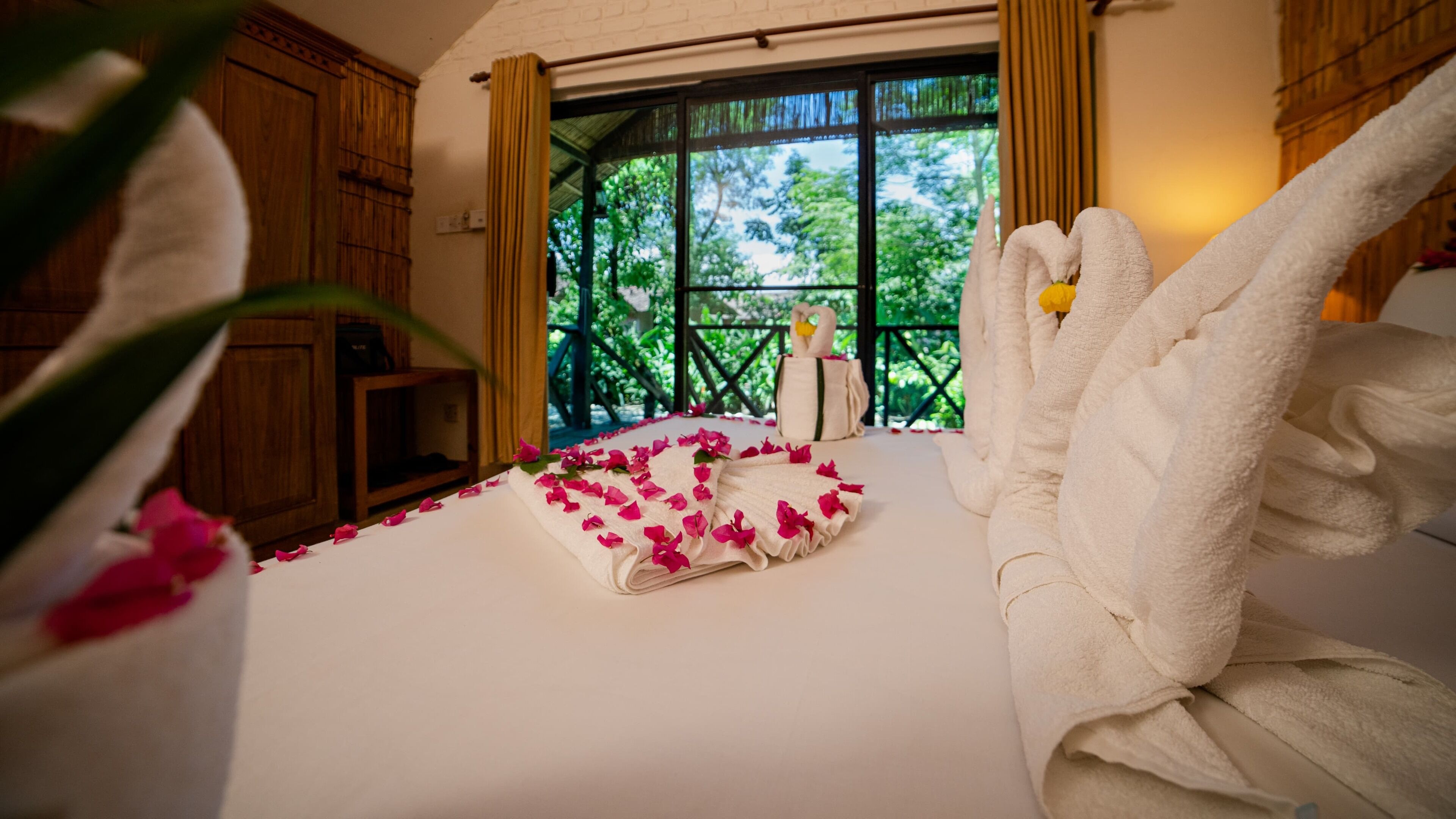 A hotel room with a bed, a window with a view of greenery, and a swan-shaped towel on the bed.