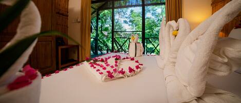 A hotel room with a bed, a window with a view of greenery, and a swan-shaped towel on the bed.