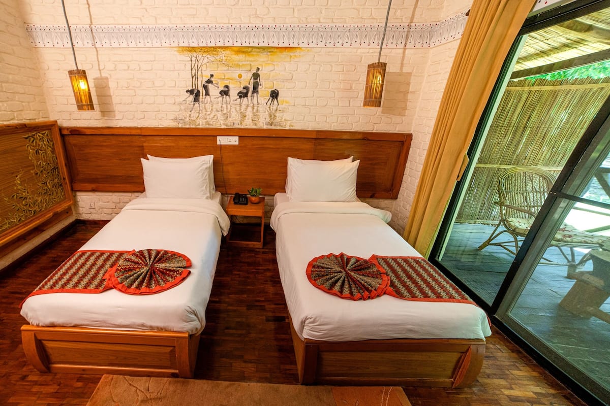 Une chambre double avec deux lits en bois, un mur en briques blanches, une fresque murale et une porte vitrée donnant sur un espace extérieur.