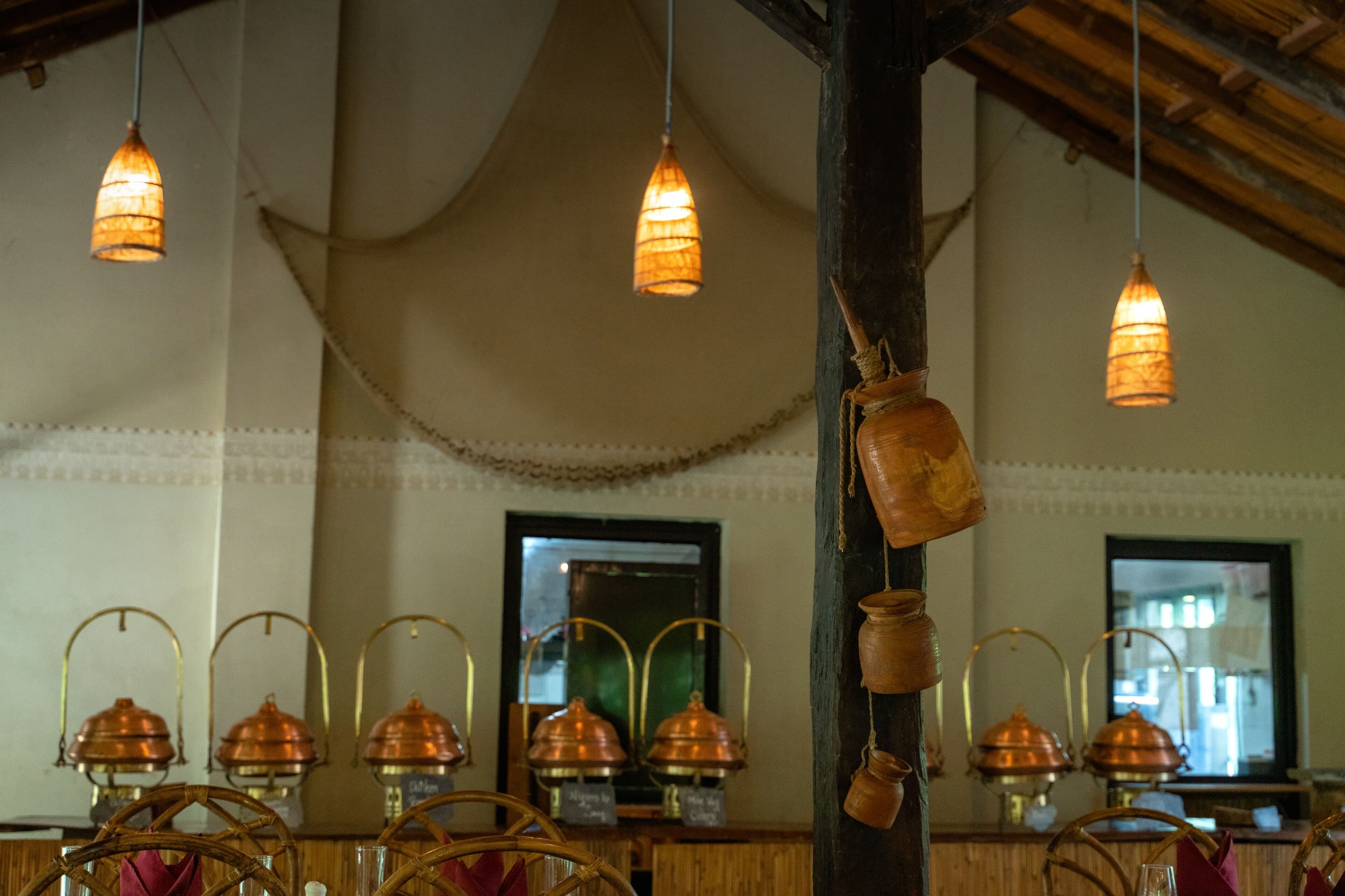 L’intérieur d’un restaurant, avec des luminaires suspendus, des casseroles en cuivre et des meubles en osier.