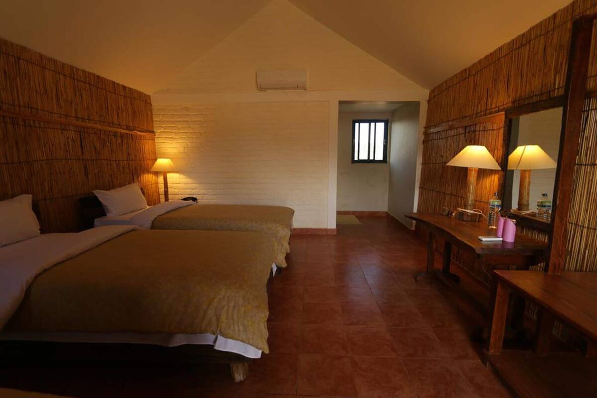 Une chambre avec deux lits, un mur en bois, une petite table avec une lampe et une fenêtre.