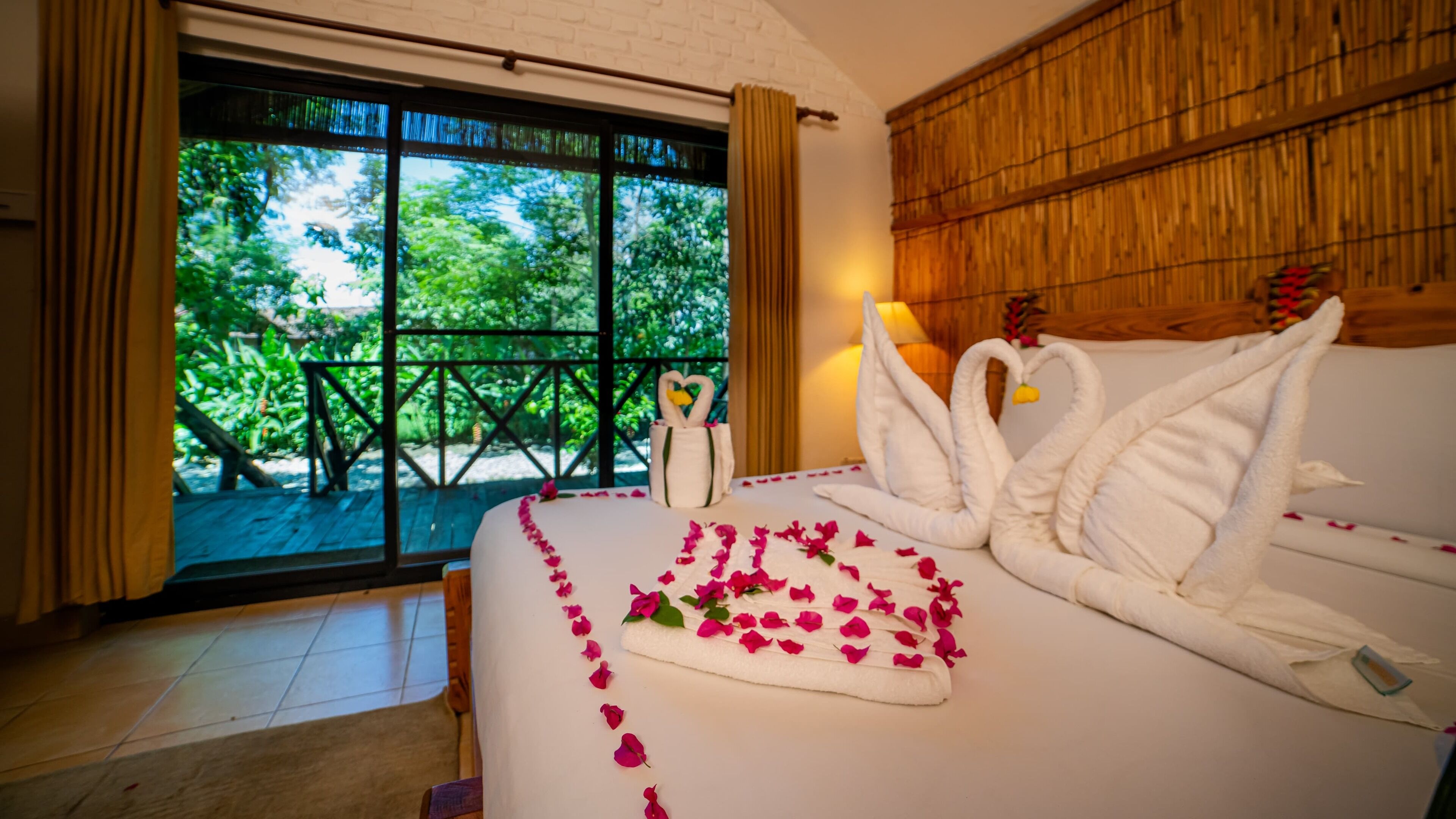 A hotel room with a bed, a window with a view of greenery, and a bamboo wall.