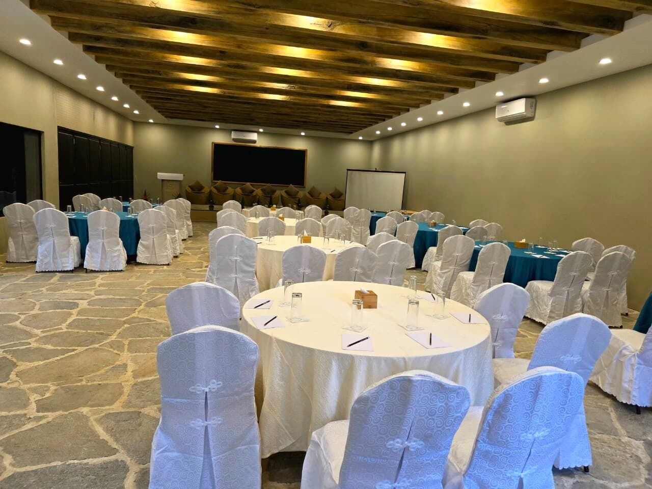 Une salle de conférence avec des tables rondes, des housses de chaise blanches et un sol en pierre.