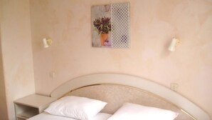 A bedroom with a bed, two nightstands, a wall-mounted light fixture, and a decorative item above the bed.