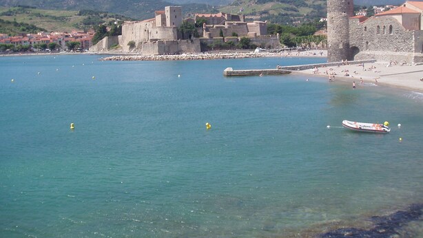 A coastal town with a prominent tower, clear blue waters, and a beach.