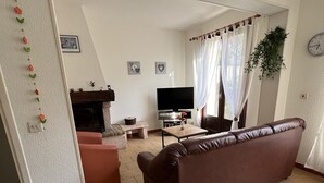 A living room with a brown sofa, a television, a fireplace, and a dining area.