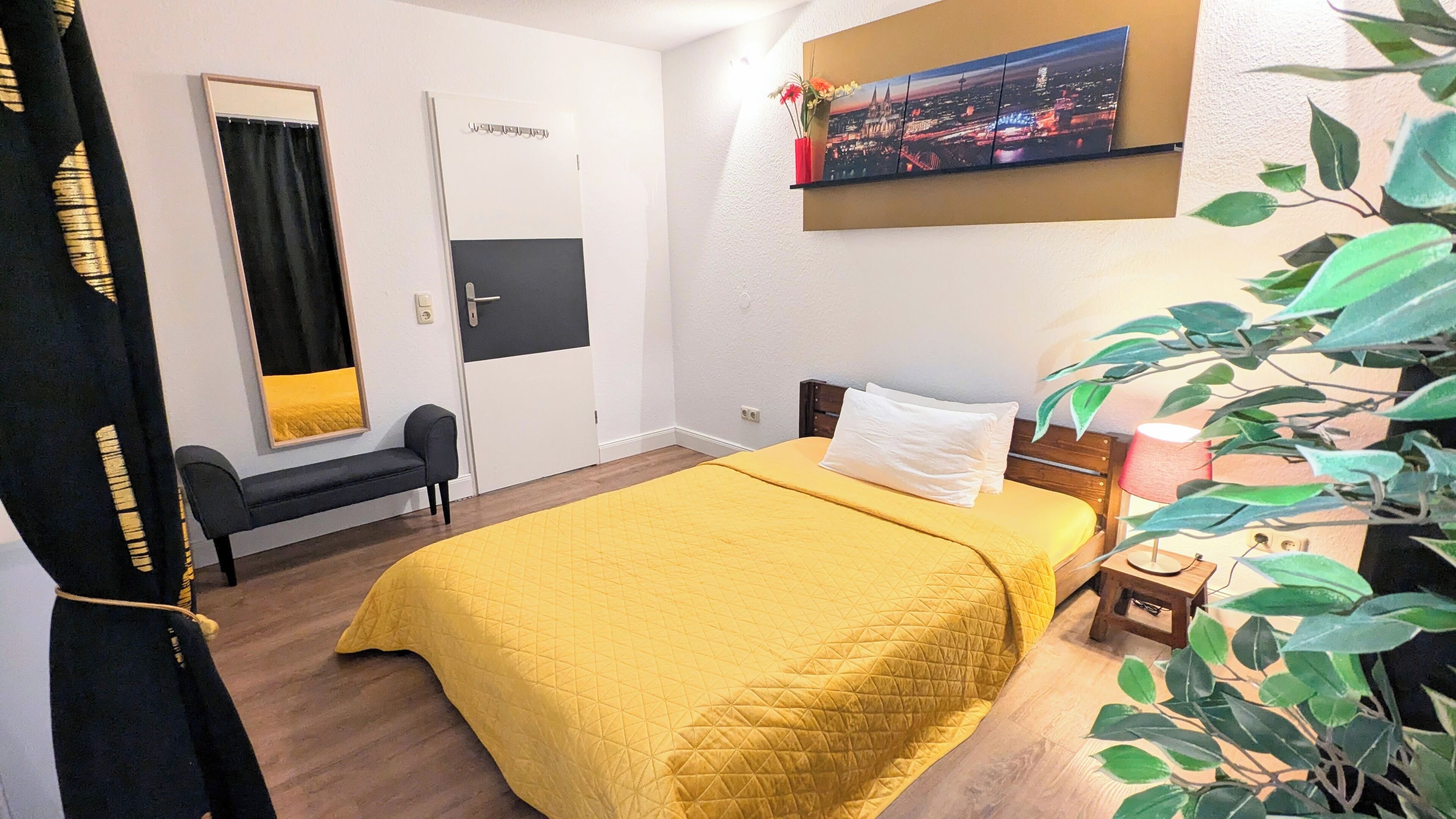 Une chambre d’hôtel avec un lit, un banc, un téléviseur fixé au mur et une plante.
