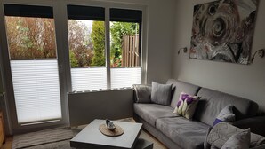A living room with a grey sofa, a coffee table, and a painting on the wall. - Vacation Bungalow Bergblüte It is awarded with 4 **** (Bad Harzburg)