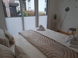 A bedroom with a large bed, a view of the outside, a small table with a plant, and a wall with dandelion decorations.