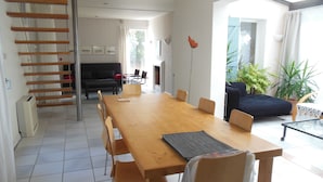 A spacious dining area with a long wooden table and chairs, a black sofa, and a staircase leading to another room. - Villa with floor and garden (Le Thoronet)
