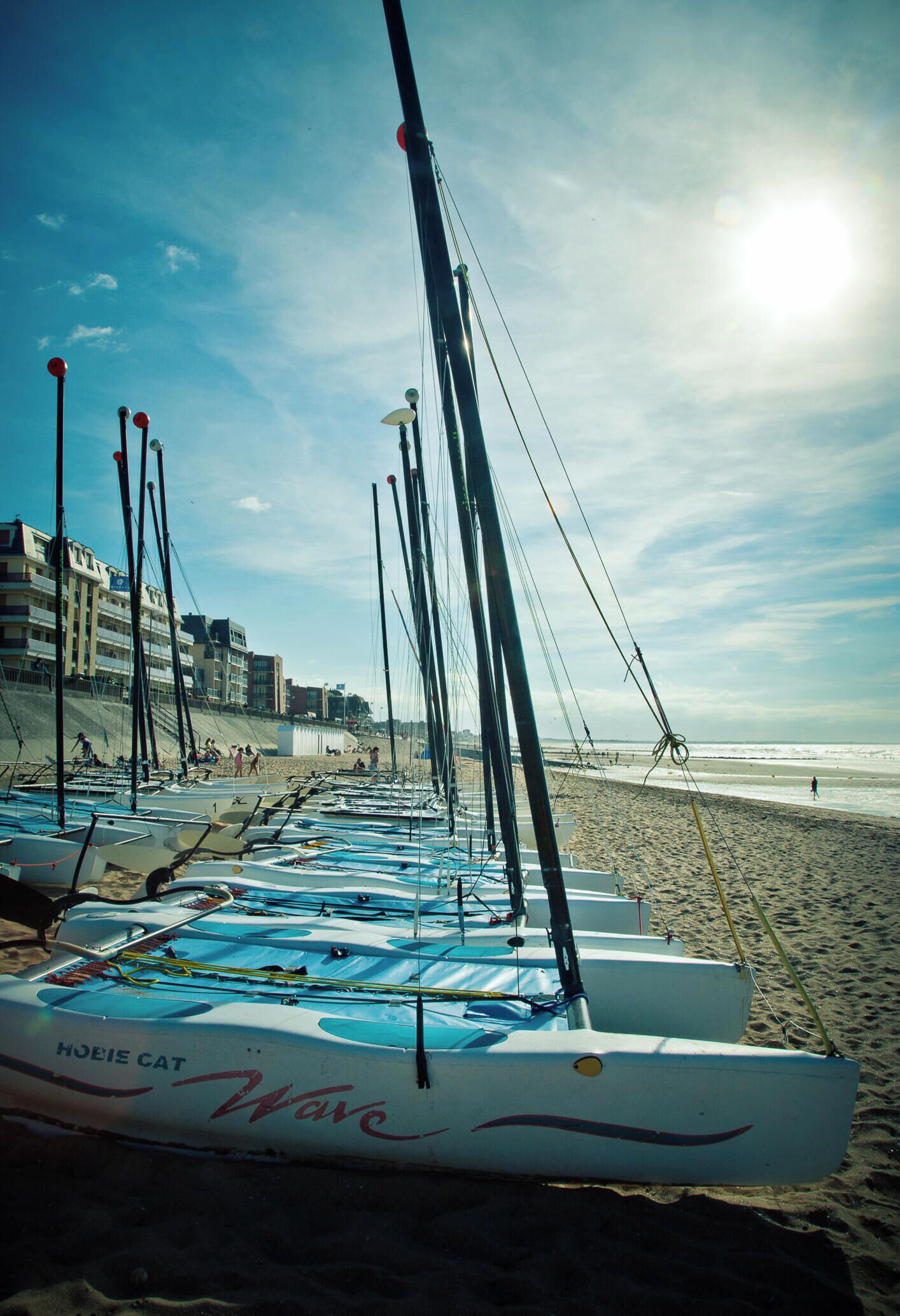 Reihenweise Boote an einem sandigen Strand, im Hintergrund Gebäude.