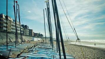 Reihenweise Boote an einem sandigen Strand, im Hintergrund Gebäude.