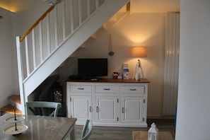 Un espace repas comprenant une table, des chaises, un téléviseur, un meuble et un escalier.