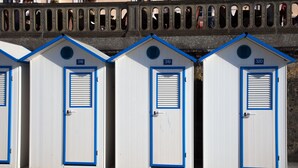 Une rangée de trois petits bâtiments modulaires blancs, avec des bordures bleues et des portes numérotées, portant les numéros 318, 319 et 320, se trouve sous un pont orné d’arches décoratives.