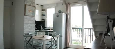 A modern kitchen with a white refrigerator, a dining table with chairs, and a balcony with a railing.