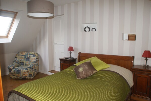 Une chambre à coucher avec un lit, une chaise, une table de chevet, une lampe, une porte et une fenêtre.