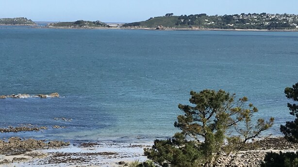 A coastal view with clear blue water, rocky shoreline, and a distant town with buildings. - HOUSE SEA VIEW 100M BEACHES WITH ENCLOSED GARDEN (Trédrez-Locquémeau)