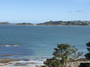 Une vue sur la côte, avec une eau d’un bleu limpide, un rivage rocheux et une ville lointaine parsemée de bâtiments.