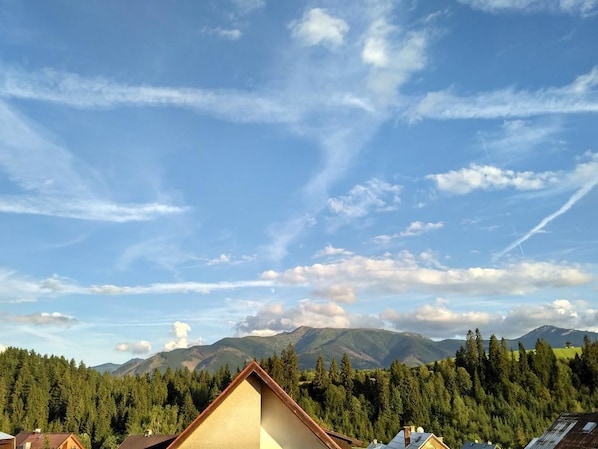 Paisaje montañoso con cielo despejado y una casa en primer plano.