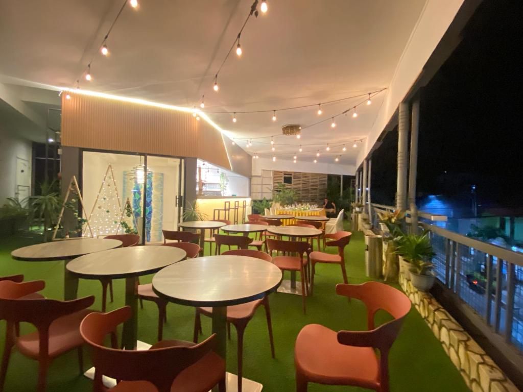 An indoor dining area with round tables and chairs, a green carpet, and string lights.