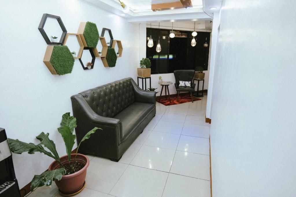 A modern interior with a black leather sofa, hexagonal wall decorations, and a dining area with chairs and hanging lights.